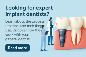 An oral and maxillofacial surgeon standing next to a chairside dental assistant, both wearing surgical scrubs and masks, consulting over digital 3D X-ray images of a patient's mouth on a computer screen. No text on the image.