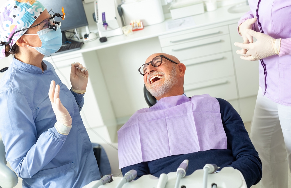 Photo of a concerned young adult looking at a bill for wisdom teeth removal, with a dentist and dental assistant blurred in the background. No text on image.